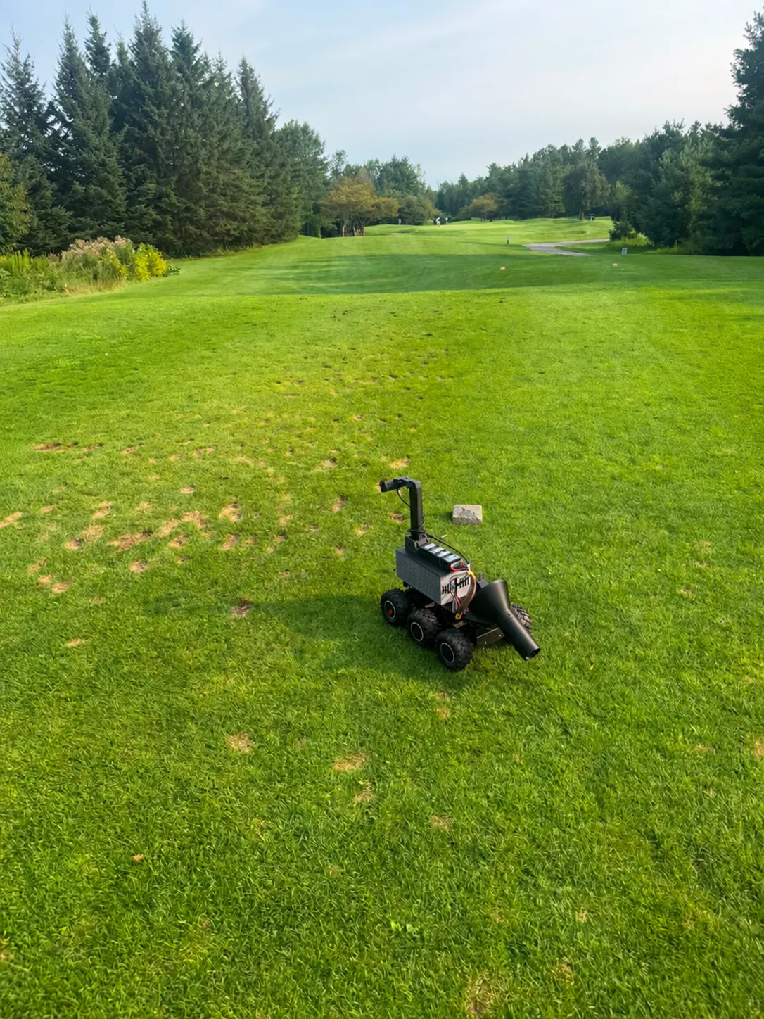 Divotron Vision, a small multi-wheeled rover with an upright tube and a front spout, on turf marked with divots